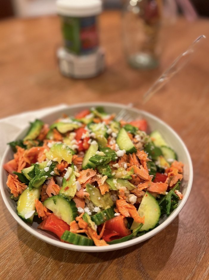 A salad of greens, cucumber, tomato, avocado, flaked salmon and feta, shared by a cohort member