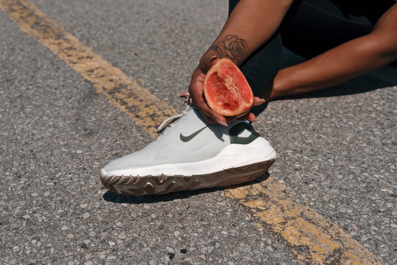 Hand holding half a grapefruit over a white sneaker on the road